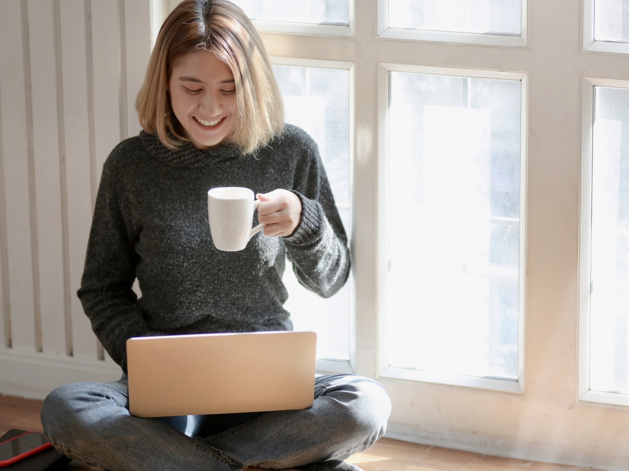 Nuori nainen tietokoneen ja kahvikupin kanssa.