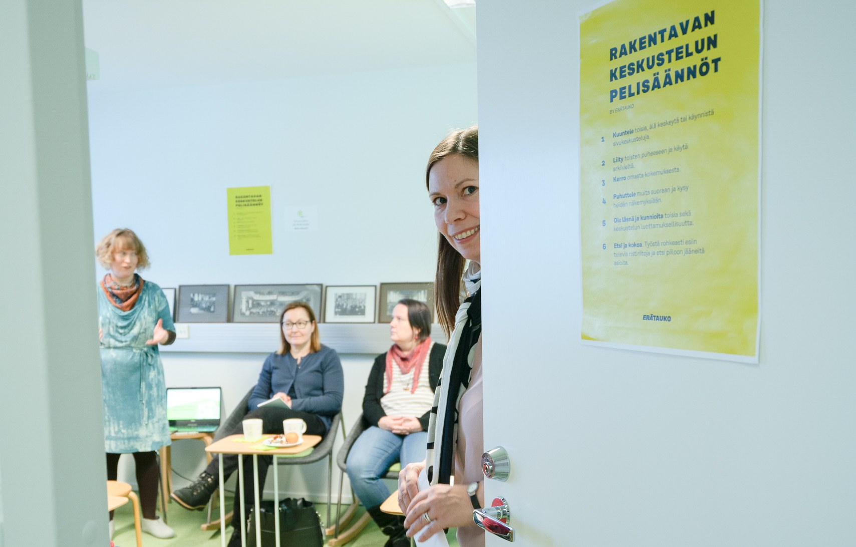 Sivis_Tervetuloa Erätaukoon Nainen avaa ovea ja toivottaa tervetulleeksi Erätauko-tilaisuuteen