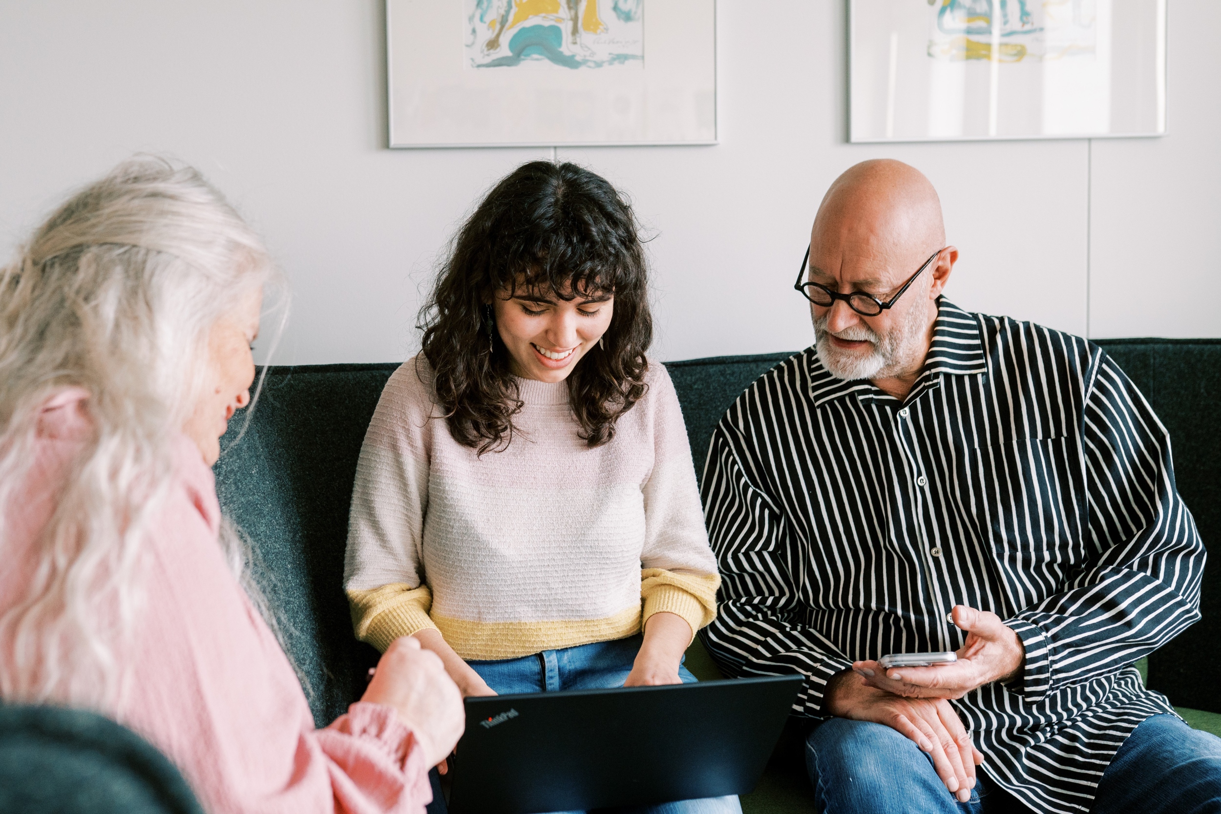 Kolme henkilöä tutkii sohvalla tietokonetta.