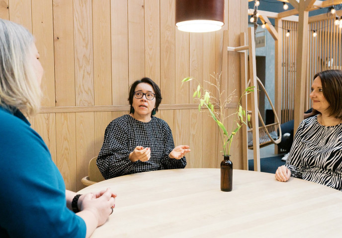 Kolme henkilöä keskustelee pöydän ympärillä.