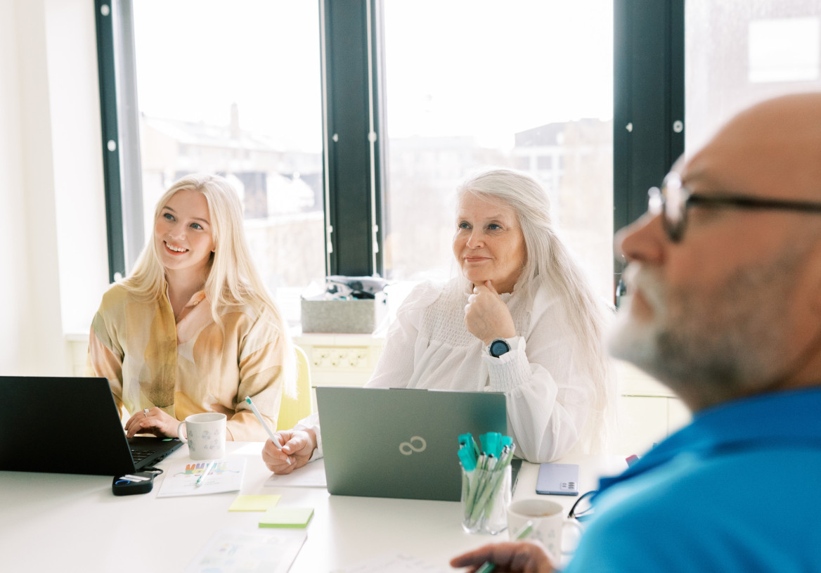 Kolme henkilöä istuu neuvotteluhuoneessa.