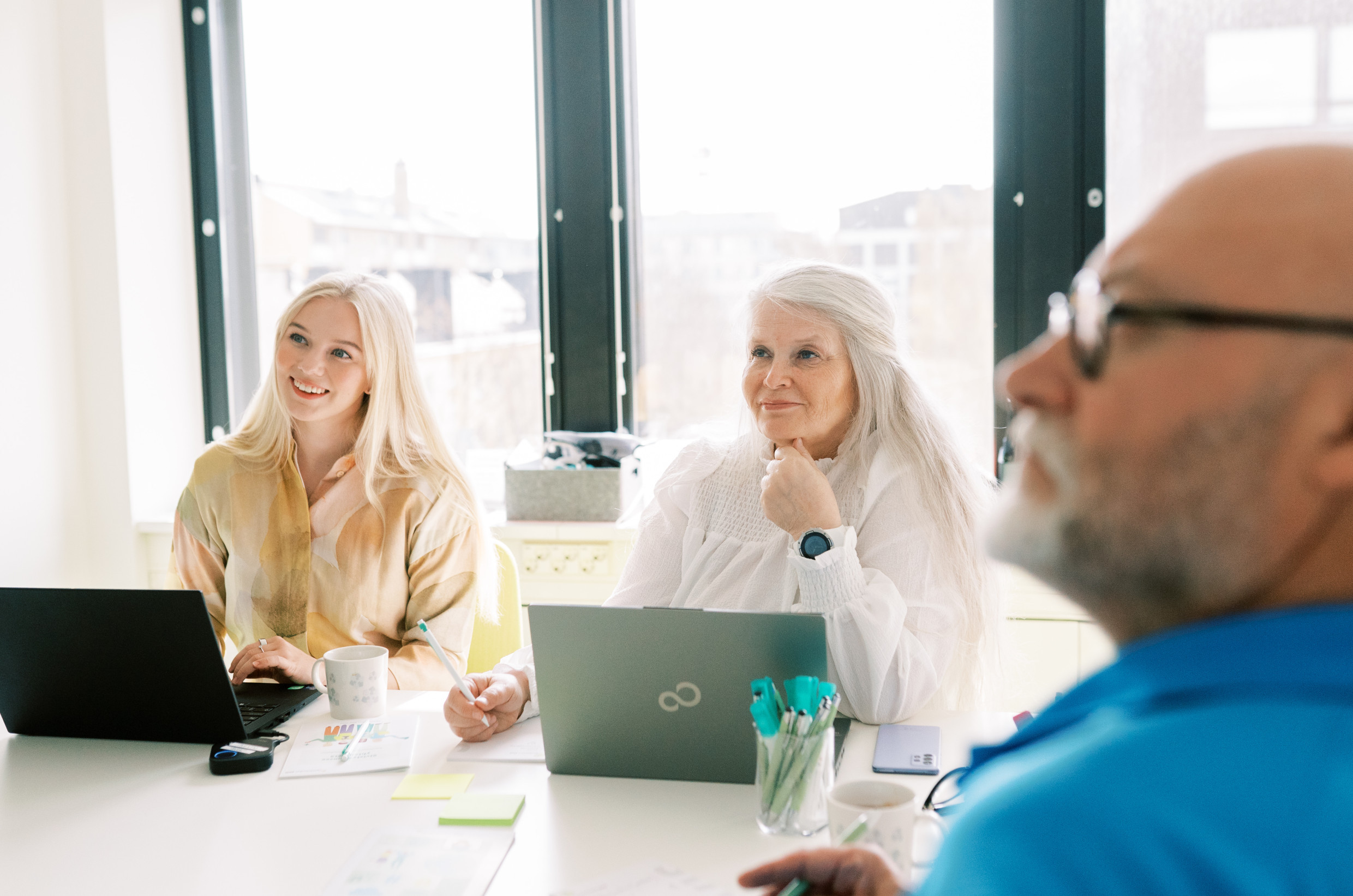 Kolme henkilöä istuu neuvotteluhuoneessa.