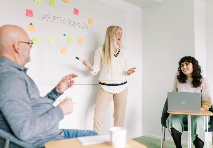 Kolme henkilöä työskentelee neuvotteluhuoneessa.